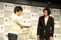 スポーツ紙に掲載されたファラオの童貞に関する記事を嬉々として紹介する新道（左）。