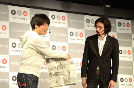 スポーツ紙に掲載されたファラオの童貞に関する記事を嬉々として紹介する新道（左）。