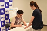 「サラリーマン山崎シゲル～THE SWORD OF GALAXY～」にサインを入れるタナカダファミリア（左）。