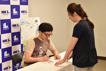 「サラリーマン山崎シゲル～THE SWORD OF GALAXY～」にサインを入れるタナカダファミリア（左）。