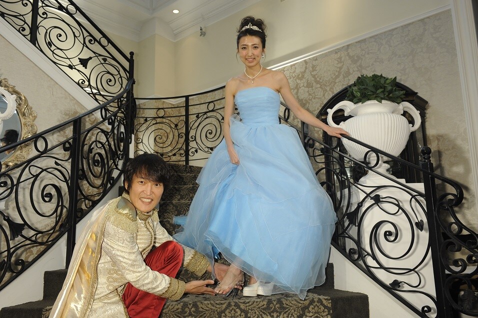 「足裏美人シンデレラ お披露目イベント」で、田幸春菜さんにガラスの靴を履かせる千原ジュニア。