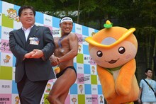 ボディビルのポージングを披露する藤本正人所沢市長、オードリー春日、所沢のマスコットキャラクター・ところん（左から）。