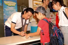 「ルミネtheよしもと フリーライブ2015 夏～ラジオ体操と笑いの祭典～」に参加した子供たちのスタンプカードにハンコを押す大山英雄。(c)吉本興業