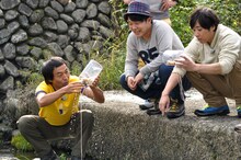 仕掛けを使って川魚を捕るペナルティ・ワッキーと、ペナルティ・ヒデ、ライセンス藤原（左から）。