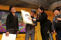 シャンプーハットこいで（左から2人目）が描いた似顔絵にコメントする今田耕司（左から3人目）。