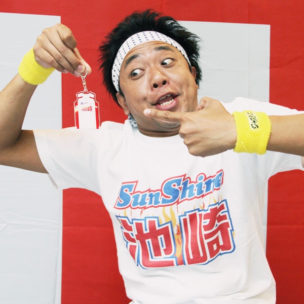 「サンシャイン池崎 Tシャツ」と「サンシャイン池崎 コスチュームキーホルダー」を身に付けたサンシャイン池崎。