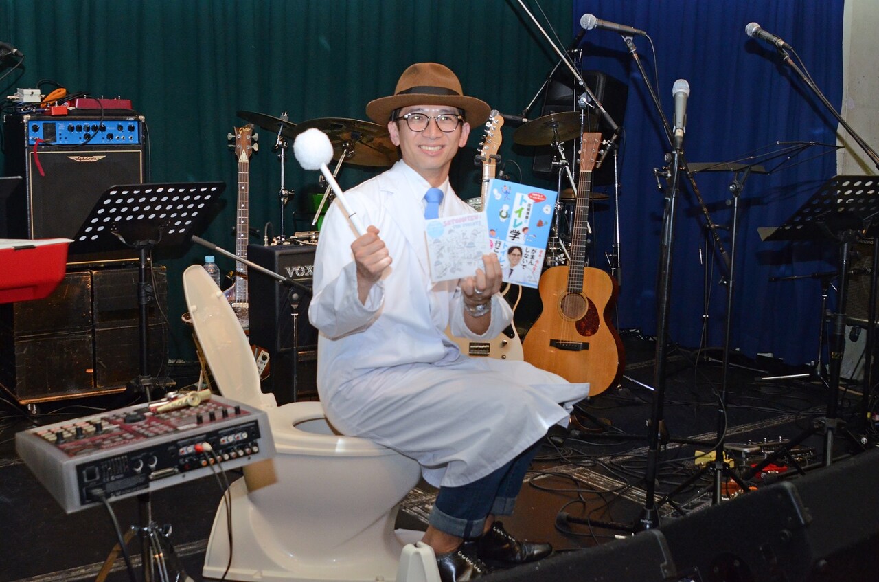 便座に腰掛けて取材陣の写真撮影に応じるどきどきキャンプ佐藤。