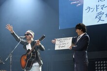 上々軍団。「ランドマークタワーで秘密のデート」を歌唱するさわやか五郎（左）と歌詞カードをめくる鈴木（右）。（写真提供：アップフロント）