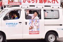 選挙カーの中から手を振るANZEN漫才みやぞん。