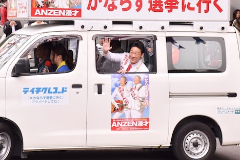 選挙カーの中から手を振るANZEN漫才みやぞん。