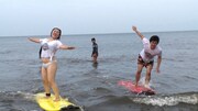 サーフィンに挑戦するフォーリンラブ・バービー(左)、平成ノブシコブシ徳井(右)。(c)HBC