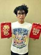 グッズのTシャツを着用し、巾着袋を持つ片桐仁。