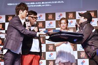 壇上でドミノ・ピザの配達を受け取るとろサーモン（左）。