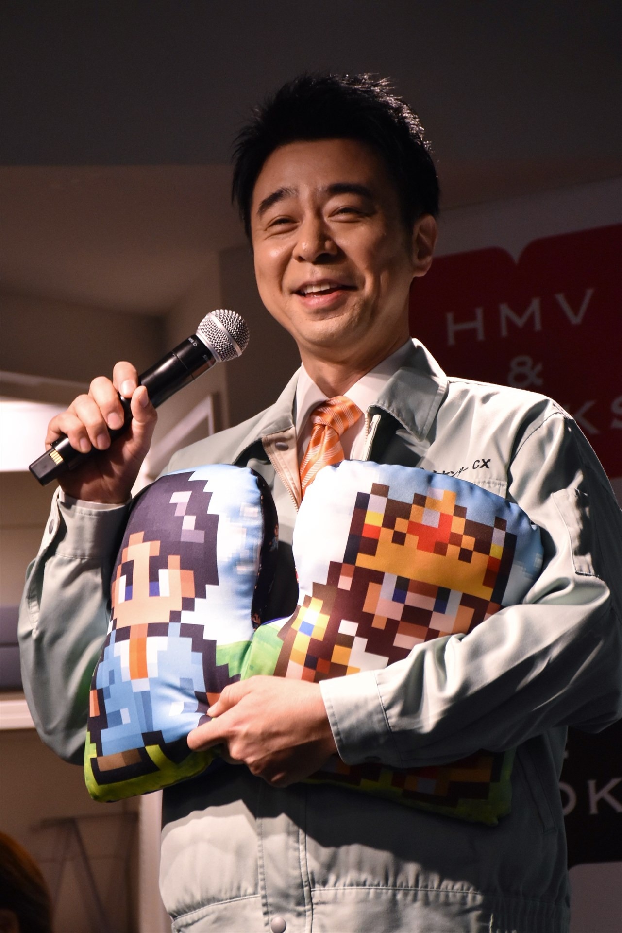展示イベント「ゲームセンターCX博物館」の開催記念グッズ「ダイカットクッション」を抱える、よゐこ有野。