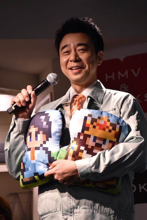 展示イベント「ゲームセンターCX博物館」の開催記念グッズ「ダイカットクッション」を抱える、よゐこ有野。