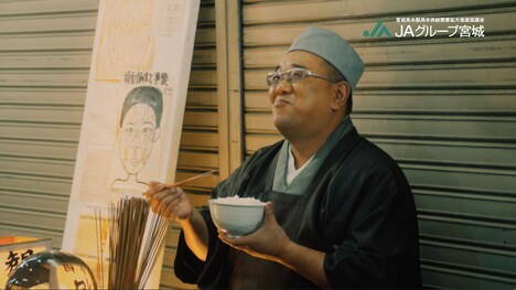 サンドウィッチマンが出演する宮城⽶の新CMより、ごはんを食べる易者役の伊達。