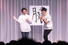 「腱」という字の前でポーズを決める祇園。