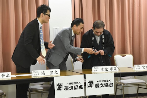 会見で話し始めようとするとマイクの一部が取れてしまう青空球児（右）。