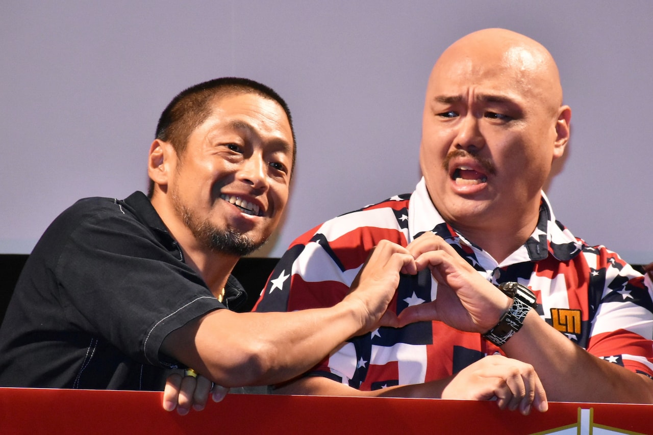 写真撮影の際、団長安田（左）が指でハートマークを作るよう求めて、クロちゃん（右）が渋々応じたワンシーン。