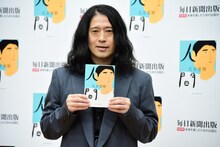 「人間」を手に、フォトセッションに応じるピース又吉。