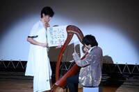ハープ演奏中の高佐に「巨人あるある」を見せつける尾関（左）。