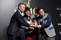 西川昌宏編集長からトロフィーを受け取るミキ昴生（右）と2人の間からひょっこり顔を出す亜生。