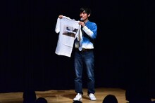 「森本ドキュメントTVコメント大賞」の受賞者に贈るTシャツを紹介するトンツカタン森本。