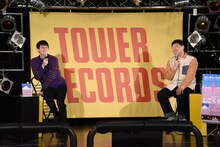 配信開始に間に合わなそうになり慌てて席に戻ったため、不安定な座り方になるロングコートダディ堂前（左）。