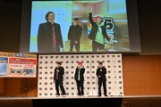 新店舗を訪問した様子が会場スクリーンに上映されたワンシーン。