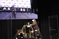 仮想空間のステージで漫才を披露する見取り図。リリーの攻撃は盛山に当たっていない。