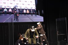 仮想空間のステージで漫才を披露する見取り図。リリーの攻撃は盛山に当たっていない。