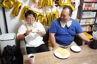 カスタードアップルピザを食べる檜原さん（左）と、その様子を見守る大鶴肥満さん（右）。