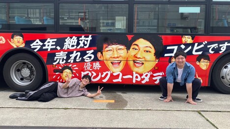 自身がデザインされたラッピングバスの前で記念撮影するロングコートダディ。(c)MBS