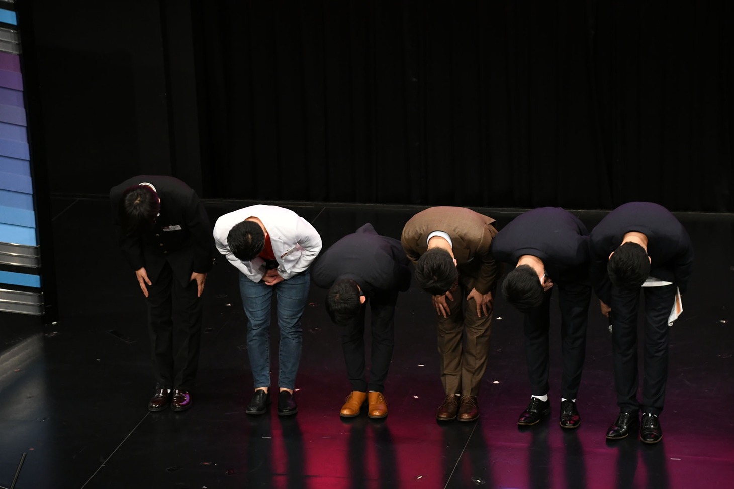 一列になって集計システムの不備を謝罪するケビンス、ダンビラムーチョ、ダイタク。