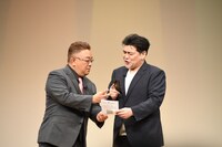 QRコードを読み込もうとする富澤のカメラにピースを写り込ませる伊達。