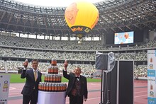 気球をバックに「健康ミネラルむぎ茶」を掲げる（左から）黒岡雅康氏、笑福亭鶴瓶。