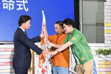 港浩一社長からフラッグを受け取る千鳥。