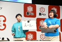 口の中がいっぱいでしゃべれないため、ボードでコメントするヨネダ2000誠。「んーんー（おいしい）」とのこと。