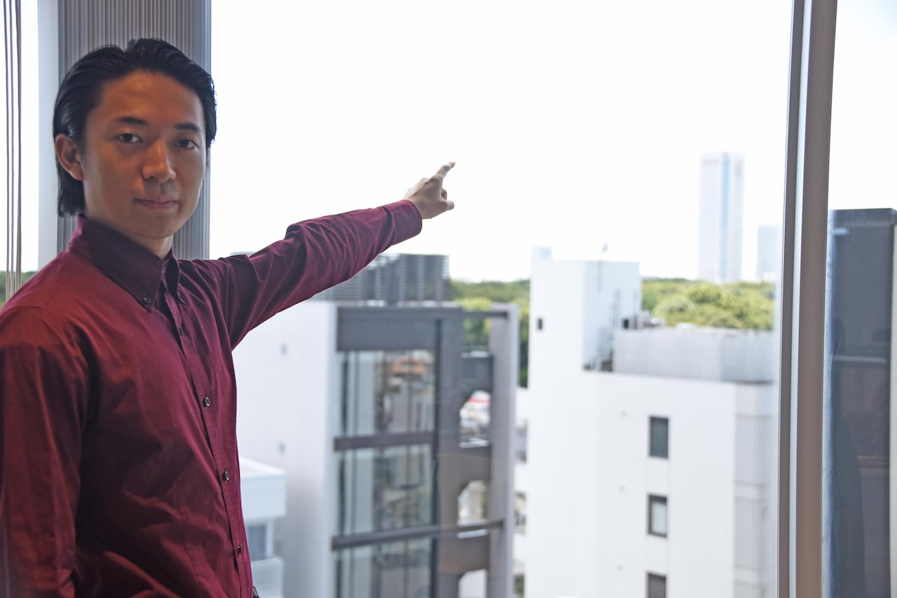 窓から見える一番高いビルを指差す友田オレ。