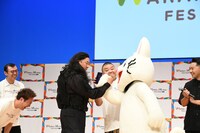 チンギスと公安・野崎のように握手を交わすレイザーラモンRGとノンタン、うしろはスマホの翻訳アプリを見せるドラム役の川畑泰史。