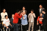 芸人詐称を疑うサルゴリラ赤羽の口を大きな手で覆って真空のような状態にしてみせる、や団・ロングサイズ伊藤。