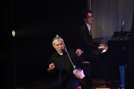 アサラトを演奏するのに頭から垂れている紐が邪魔そうな塚本。