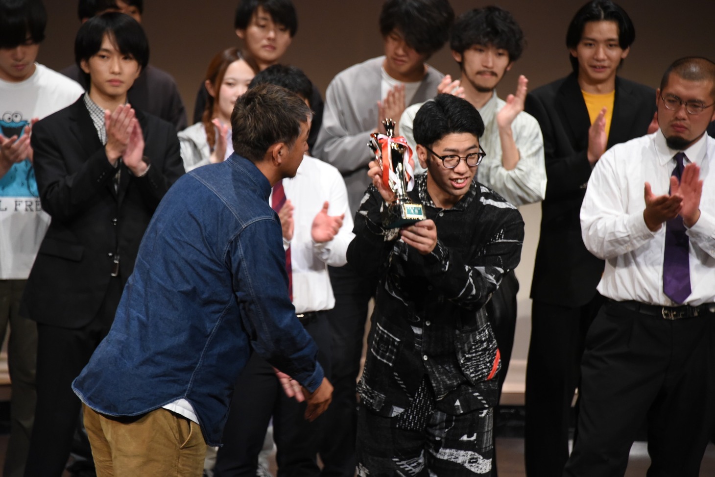 トロフィーを受け取る鯖のTシャツ・カンドウ。