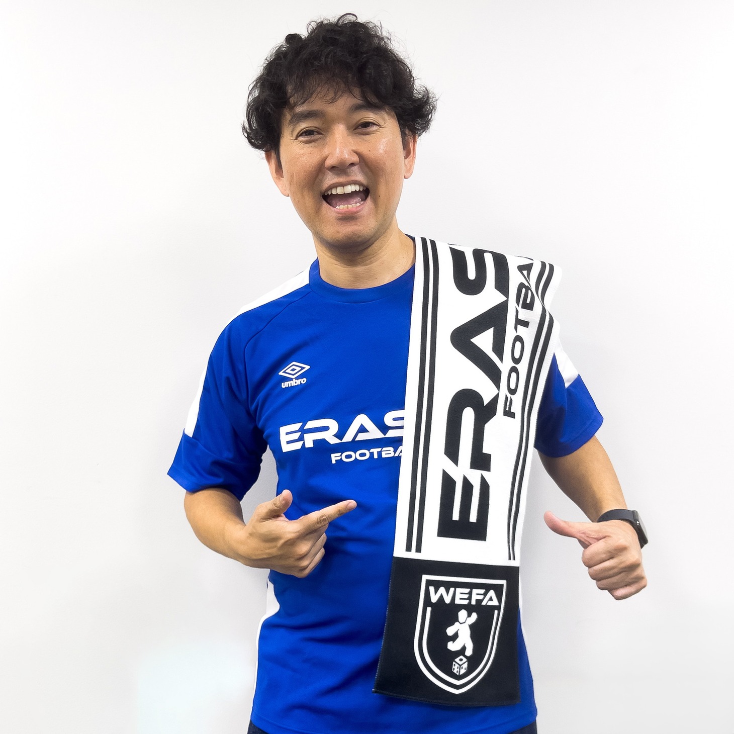 「消しサカ ユニフォーム」を着用し、「消しサカ マフラータオル」を肩にかけたナイツ土屋。
