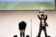 トロフィーを掲げるツートライブ周平魂（右）と深々とお辞儀するたかのり（左）