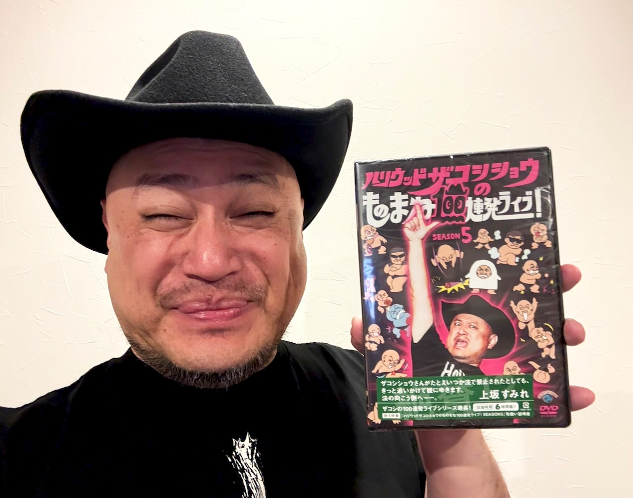 DVD「ハリウッドザコシショウのものまね100連発ライブ！SEASON5」パッケージを手にするハリウッドザコシショウ