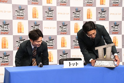 会見場に入場後、トロフィーをテーブルのギリギリに置こうとするトット桑原