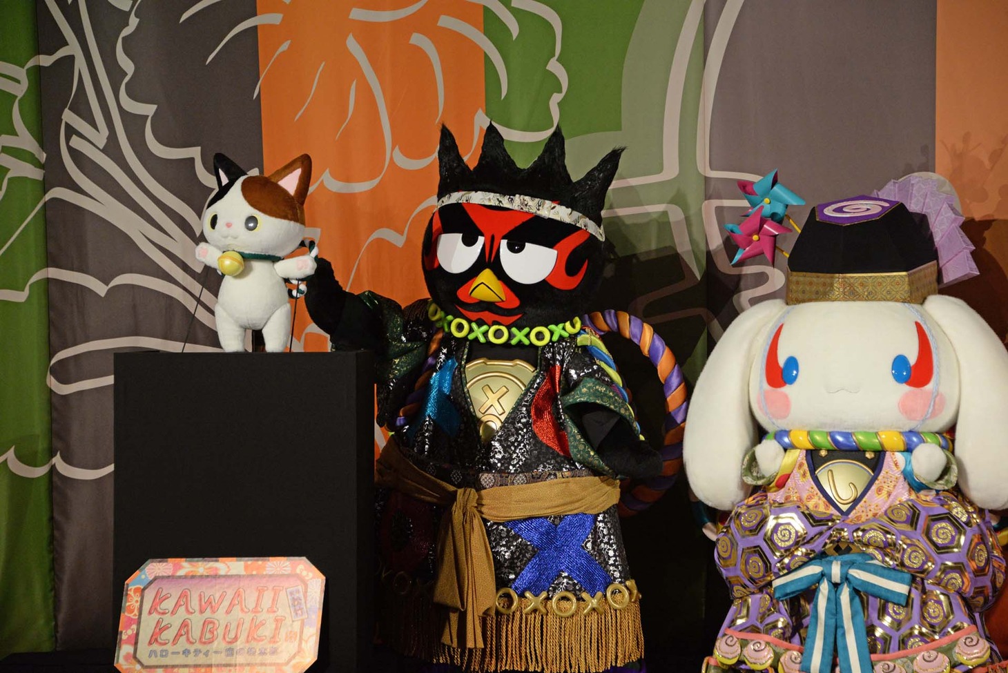 「KAWAII KABUKI～ハローキティ一座の桃太郎～」記者発表会より、かぶきにゃんたろう（左）とハイタッチしようとするバッドばつ丸（中央）。