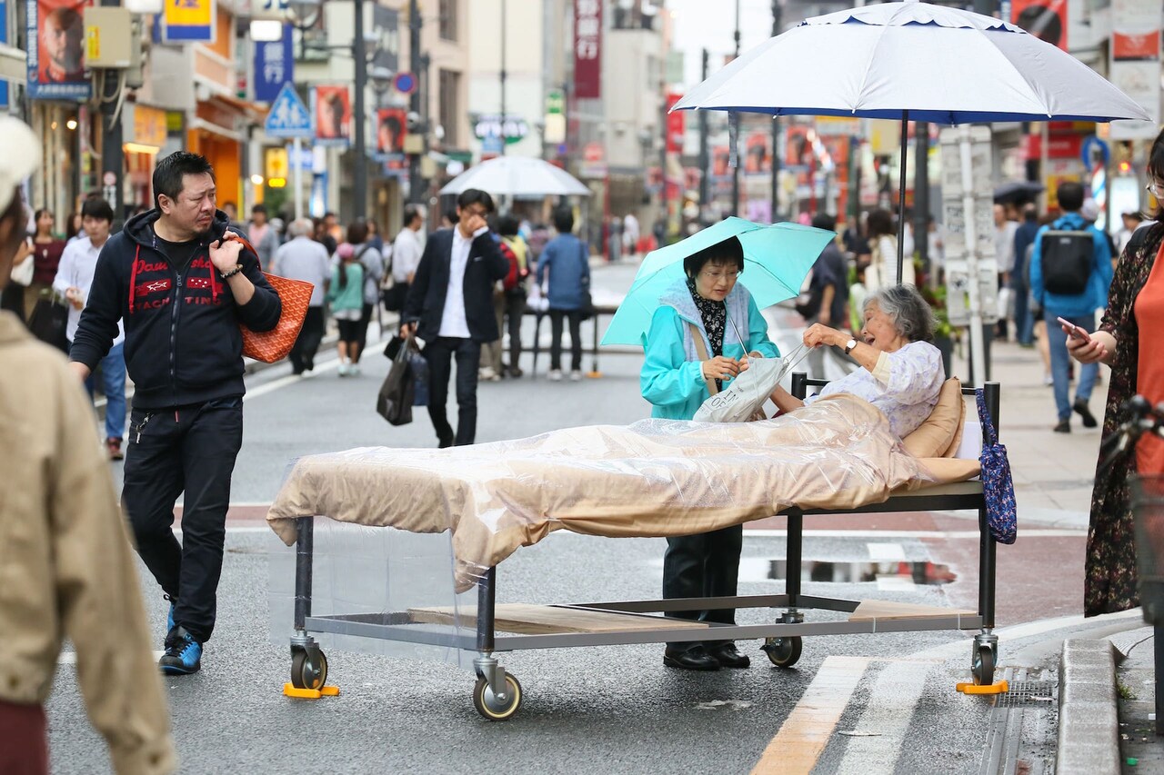 突如街角に現れるベッド、老人たちが通行人に語りかける「BED」