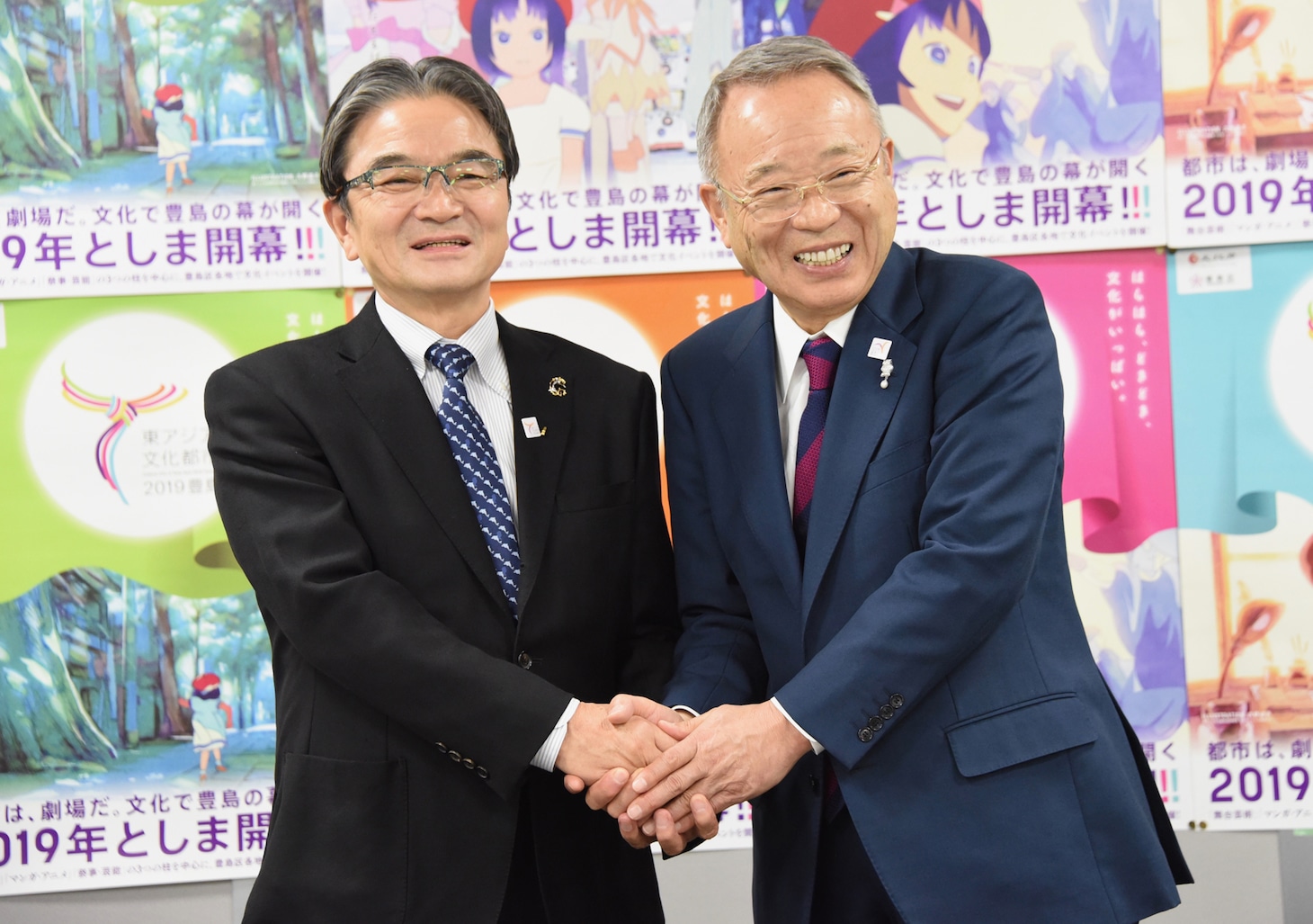「東アジア文化都市2019豊島」文化庁・豊島区共同記者会見より、握手を交わす宮田亮平氏（左）と高野之夫氏（右）。